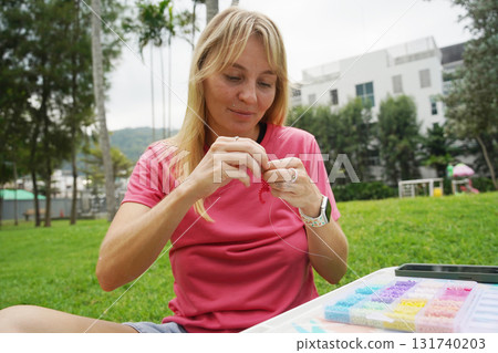 Young woman beading colorful bracelets outdoors in a park Young woman beading colorful bracelets outdoors in a park 131740203