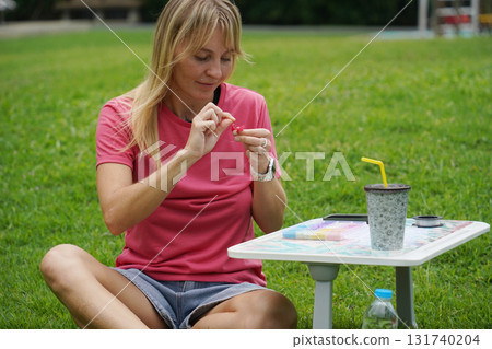Young woman beading colorful bracelets outdoors in a park Young woman beading colorful bracelets outdoors in a park 131740204