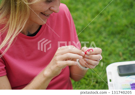 Young woman beading colorful bracelets outdoors in a park 131740205