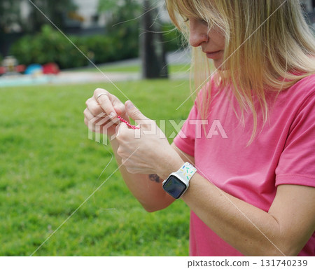 Young woman beading colorful bracelets outdoors in a park Young woman beading colorful bracelets outdoors in a park 131740239