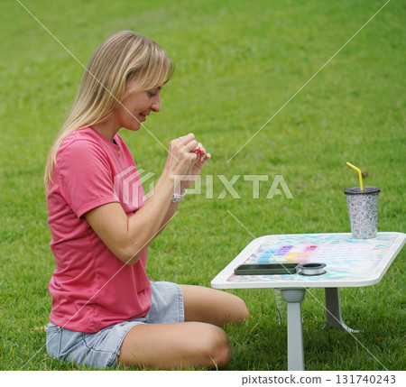 Young woman beading colorful bracelets outdoors in a park Young woman beading colorful bracelets outdoors in a park 131740243