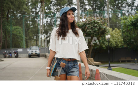A woman is walking at the city park while carrying a skateboard in her hands 131740318