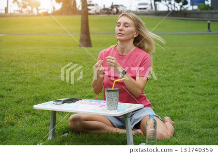 Young woman beading colorful bracelets outdoors in a park 131740359
