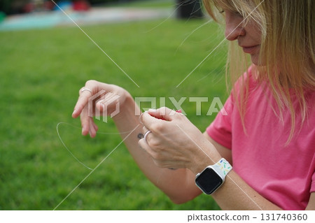 Young woman beading colorful bracelets outdoors in a park Young woman beading colorful bracelets outdoors in a park 131740360