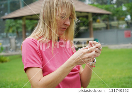 Young woman beading colorful bracelets outdoors in a park 131740362