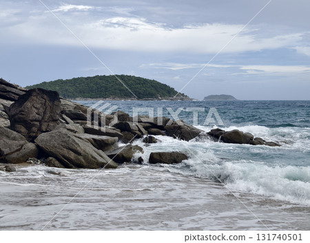 A tranquil beach scene featuring gentle waves lapping against rocks 131740501