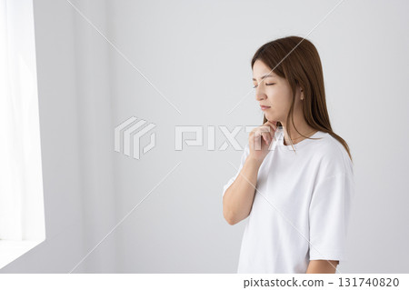 A young woman with a troubled expression in a bright room 131740820