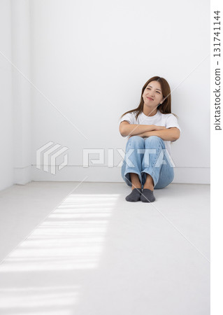Smiling young woman sitting on the floor in a bright room with light coming in through the window Smiling young woman sitting on the floor in a bright room with light coming in through the window 131741144