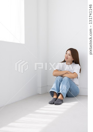 微笑的年輕女子坐在明亮房間的地板上，光線透過窗戶照進來 131741146