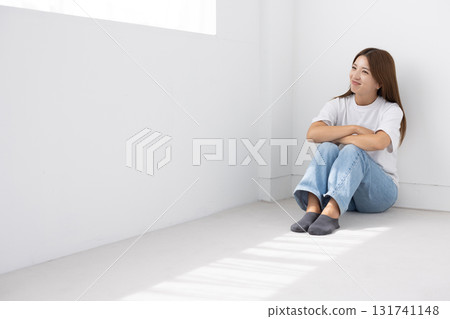 微笑的年輕女子坐在明亮房間的地板上，光線透過窗戶照進來 131741148