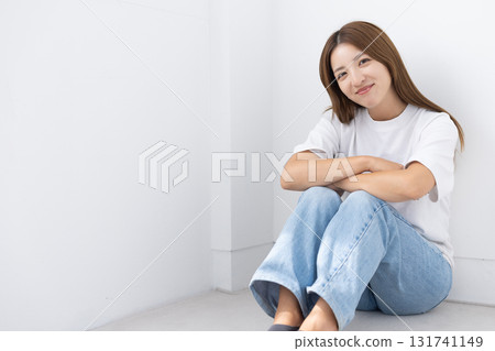 微笑的年輕女子坐在明亮房間的地板上，光線透過窗戶照進來 131741149