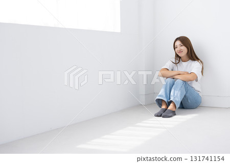 微笑的年輕女子坐在明亮房間的地板上，光線透過窗戶照進來 131741154