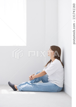 微笑的年輕女子坐在明亮房間的地板上，光線透過窗戶照進來 131741160