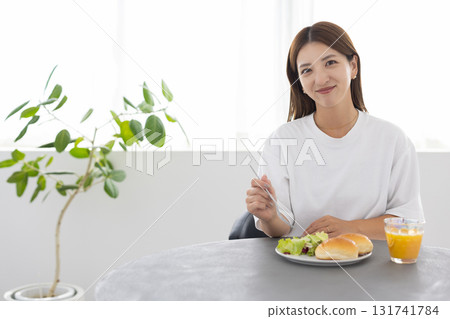 一位年輕女子在明亮的房間裡享用健康早餐，陽光透過窗戶照進來 131741784