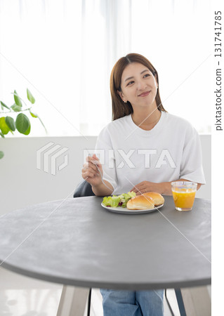 一位年輕女子在明亮的房間裡享用健康早餐，陽光透過窗戶照進來 131741785