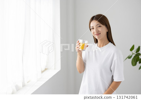 一位年輕女子在明亮的窗邊拿著一杯柳橙汁 131742061