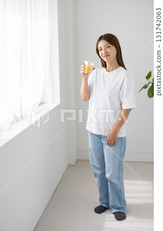 一位年輕女子在明亮的窗邊拿著一杯柳橙汁 131742063