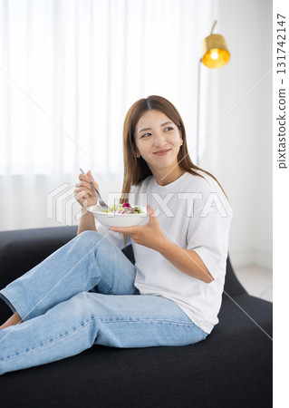 年輕女子坐在沙發上吃蔬菜沙拉 131742147