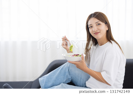 Young woman sitting on sofa and eating vegetable salad Young woman sitting on sofa and eating vegetable salad 131742149