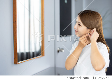 Young woman putting on earrings in front of a mirror 131742238