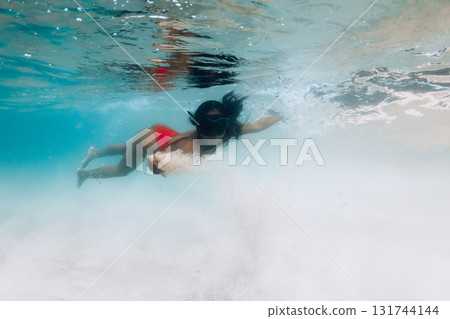 Woman in red swimsuit and mask glides underwater in tropical waters with sandy sea bottom Woman in red swimsuit and mask glides underwater in tropical waters with sandy sea bottom 131744144