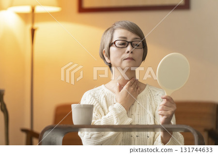 Senior woman looking at a hand mirror in the living room at night 131744633