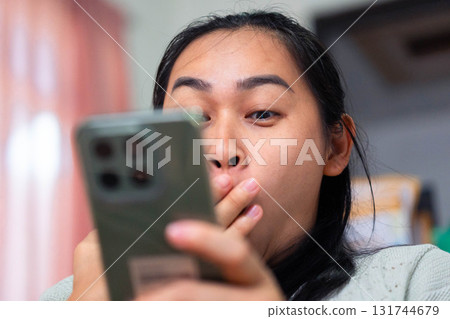 Asian Woman Shocked and Covering Mouth While Looking at Smartphone 131744679