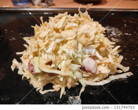 Traditional Japanese okonomiyaki being cooked on a teppan grill, showing delicious texture and authentic street food style. 131744783
