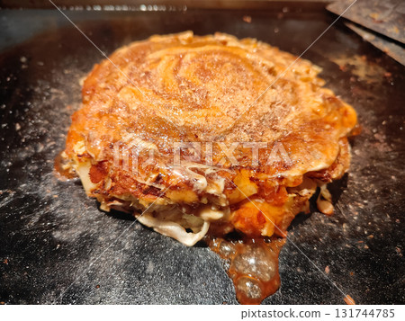 Traditional Japanese okonomiyaki being cooked on a teppan grill, showing delicious texture and authentic street food style. 131744785