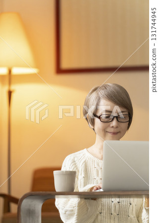 晚上，老年婦女在客廳裡用筆記型電腦聊天和閱讀 131744945