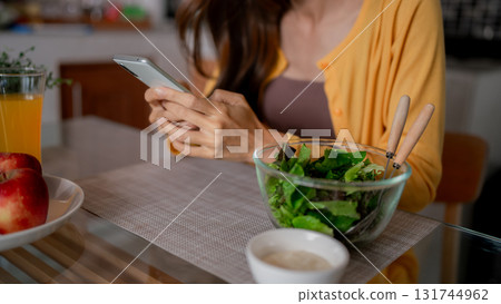 Asian adult woman enjoy healthy meal home casual browse smartphone digital communication technology fresh green salad Asian adult woman enjoy healthy meal home casual browse smartphone digital communication technology fresh green salad 131744962