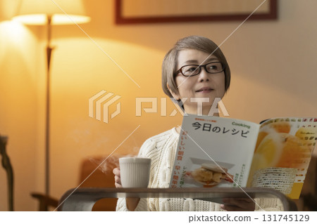 Senior woman looking at a recipe book in the living room at night Senior woman looking at a recipe book in the living room at night 131745129