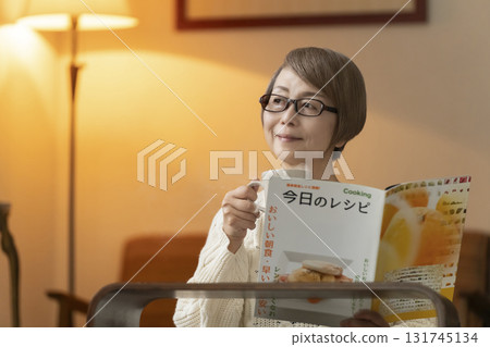 Senior woman looking at a recipe book in the living room at night Senior woman looking at a recipe book in the living room at night 131745134