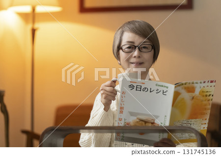 Senior woman looking at a recipe book in the living room at night 131745136