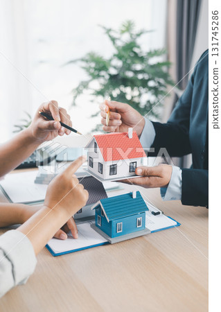 Close up of real estate agent showing small house model to client with calculator, contract paperwork on desk, concept of mortgage loan, home ownership, property investment agreement. mortgage loan Close up of real estate agent showing small house model to client with calculator, contract paperwork on desk, concept of mortgage loan, home ownership, property investment agreement. mortgage loan 131745286
