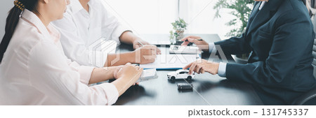 Panorama view of business meeting with car loan agreement, dealer showing calculator to customers at office desk with vehicle model and key, concept of auto finance, leasing or insurance. car loan. 131745337