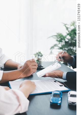 Businessman explaining car loan agreement with calculator, customer discussing auto finance deal at office desk with toy car and document, concept of vehicle loan, insurance or car leasing. car loan. 131745439