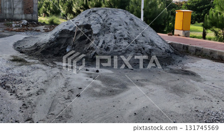 Large mound of grey sand and gravel with coarse texture in bright daylight near green foliage and yellow utility box Large mound of grey sand and gravel with coarse texture in bright daylight near green foliage and yellow utility box 131745569
