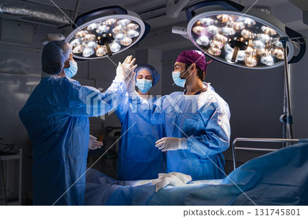 Medical team celebrates a successful procedure in a modern operating room, illuminated by surgical lights. Medical team celebrates a successful procedure in a modern operating room, illuminated by surgical lights. 131745801