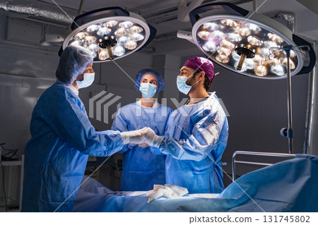 Medical team in surgical attire preparing for an operation under bright lights in a sterile operating room. 131745802