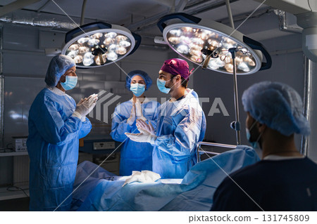 Medical team preparing for surgery in a modern operating room, illuminated by bright surgical lights. Medical team preparing for surgery in a modern operating room, illuminated by bright surgical lights. 131745809