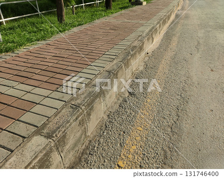 Concrete curb with exposed texture between red and tan brick sidewalk and worn asphalt road in bright daylight 131746400