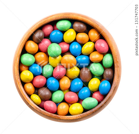 Colorful sugar-coated chocolate dragees, in a wooden bowl. Dragee chocolate confectionery consisting of a multi colored candy shell surrounding a chocolate filling. Isolated close-up from above. Photo Colorful sugar-coated chocolate dragees, in a wooden bowl. Dragee chocolate confectionery consisting of a multi colored candy shell surrounding a chocolate filling. Isolated close-up from above. Photo 131747703