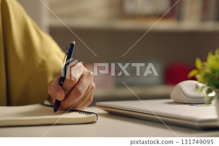 Asian woman works from home, surrounded by notes, a laptop, and messages. She browses the internet, writes ideas, and researches for her startup, utilizing wireless technology. 131749095