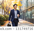 Smiling Japanese man walking through an office district in autumn - urban morning scene with close-up of his commuter style and facial expression 131749716