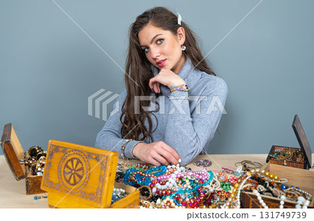 young brunette sitting at the table with lots of jewelry, choosing and trying different jewelry 131749739
