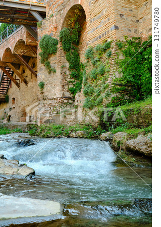 Water flows gently over rocks near a historic stone wall covered in greenery in the afternoon sun Water flows gently over rocks near a historic stone wall covered in greenery in the afternoon sun 131749780