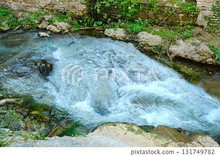 Clear river water flowing over rocks in a natural setting during daylight 131749782