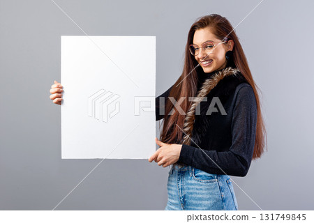 smiling young teenager woman showing blank signboard with copy space, isolated on gray 131749845