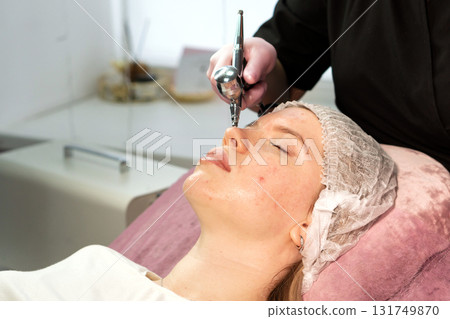 Esthetician sprays hydrating mist onto client's nose tip 131749870